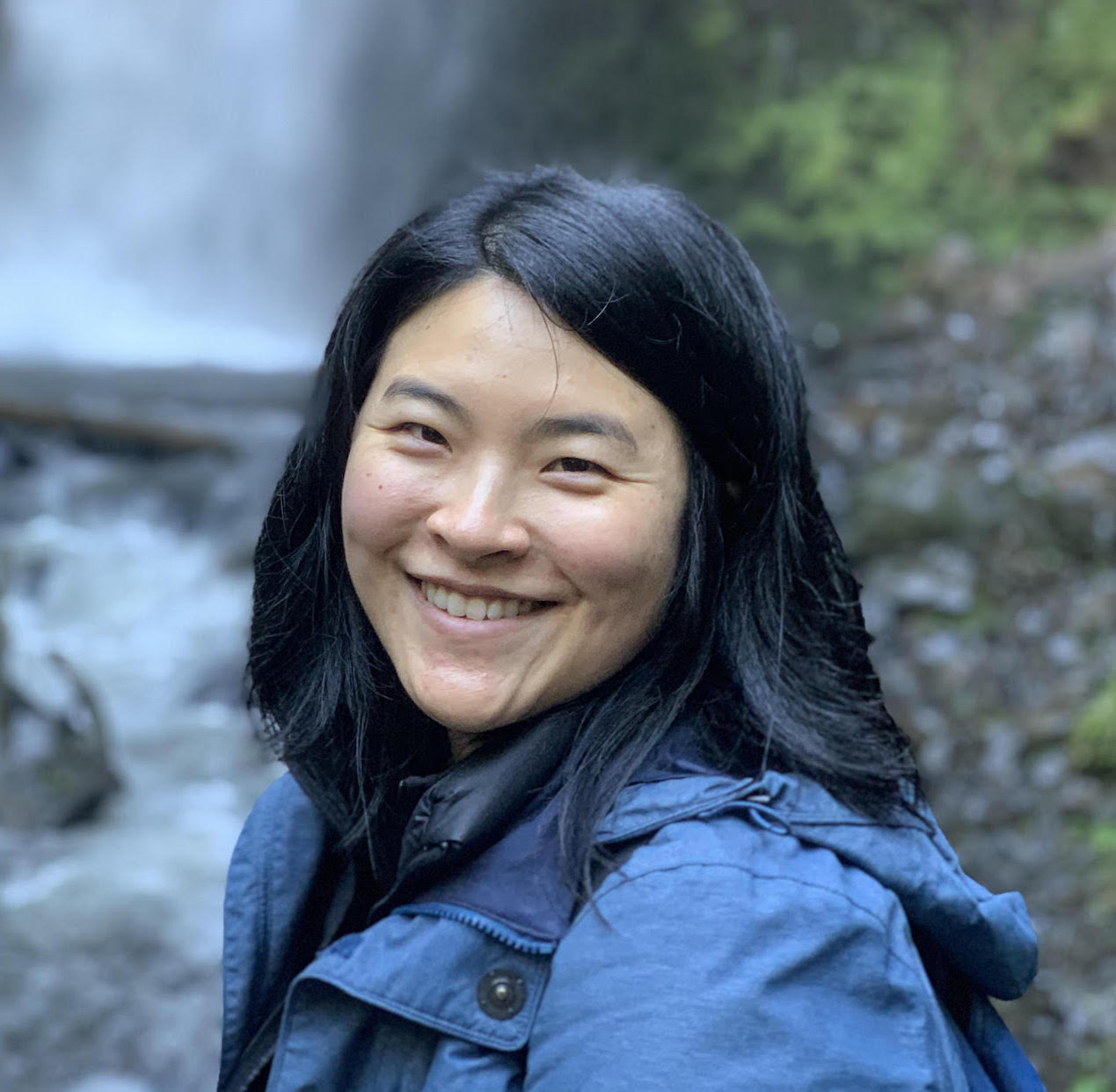 An image of Jeena Lee standing in front of a waterfall